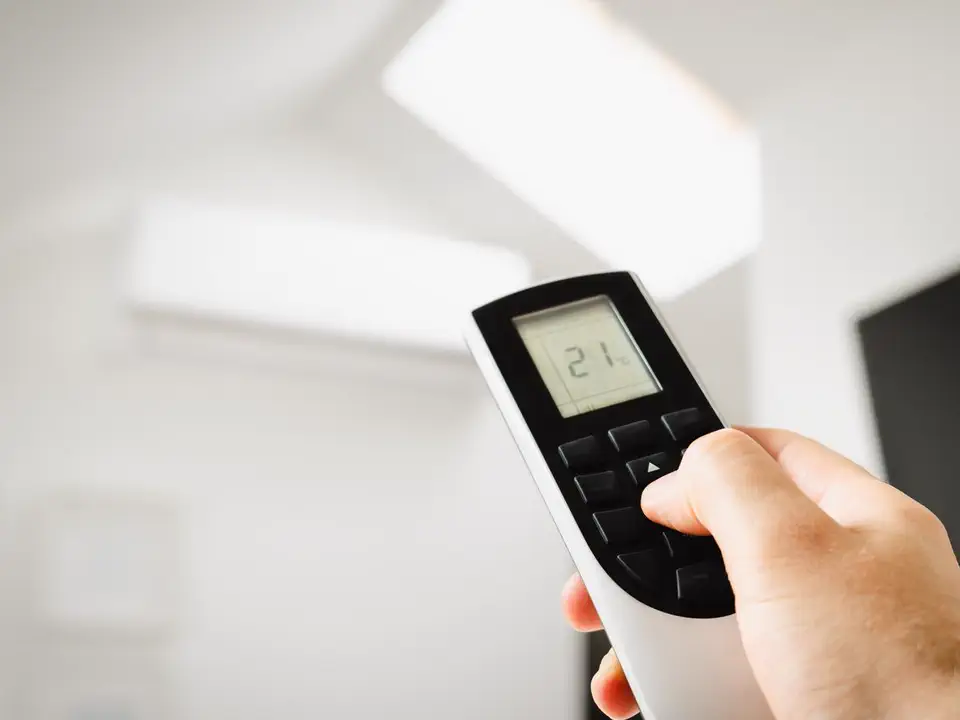A hand setting the temperature on a ductless mini-split with the wall-mounted indoor head behind it